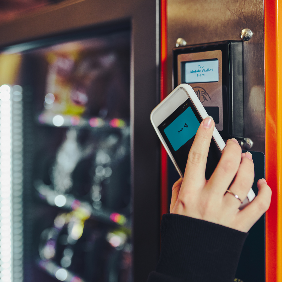 Someone paying at a vending machine by tapping a phone on the card reader